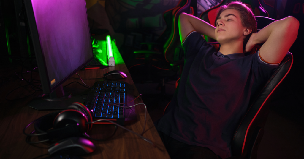 A young gamer takes a mid-session stretch beside their setup, leaning back to recharge before the next match.